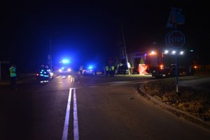 Na zdjęciu widać policyjne radiowozy i bojowe wozy strażackie z włączonymi sygnałami błyskowymizabezpieczające miejsce tragicznego wypadku drogowego. Obecni na miejscu policjanci wykonują czynności procesowe związane z wyjaśnieniem przyczyn wypadku.