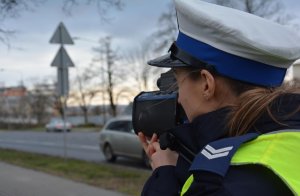 Policjantka mierzy prędkość pojazdów na drodze przy pomocy laserowego miernika prędkości
