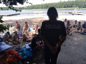 na zdjęciu widoczny funkcjonariusz policji w tle dzieci i młodzież przebywająca nad wodą