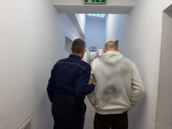 Policjant prowadzi zatrzymanego mężczyznę do celi